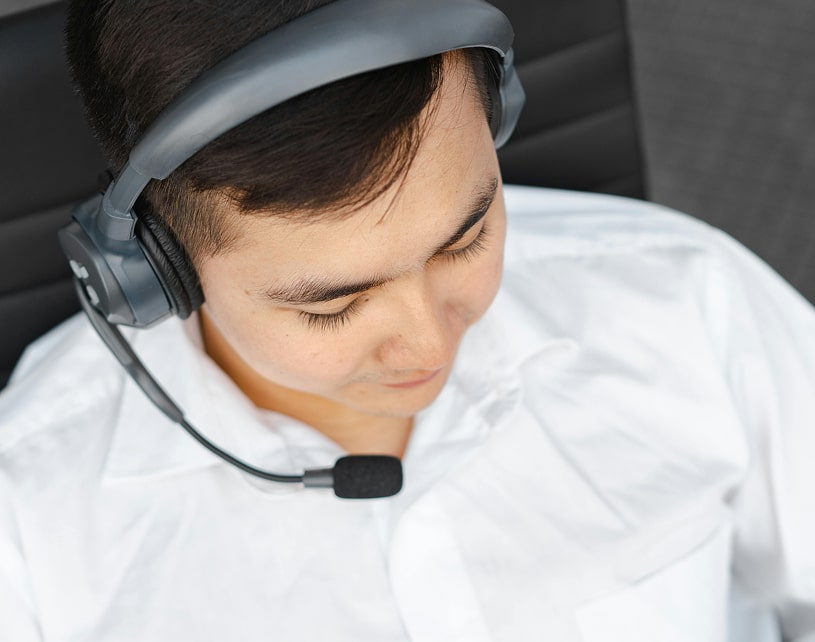 A person wearing a headset sits in a modern chair, dressed in a white shirt, focused on an off-screen task.