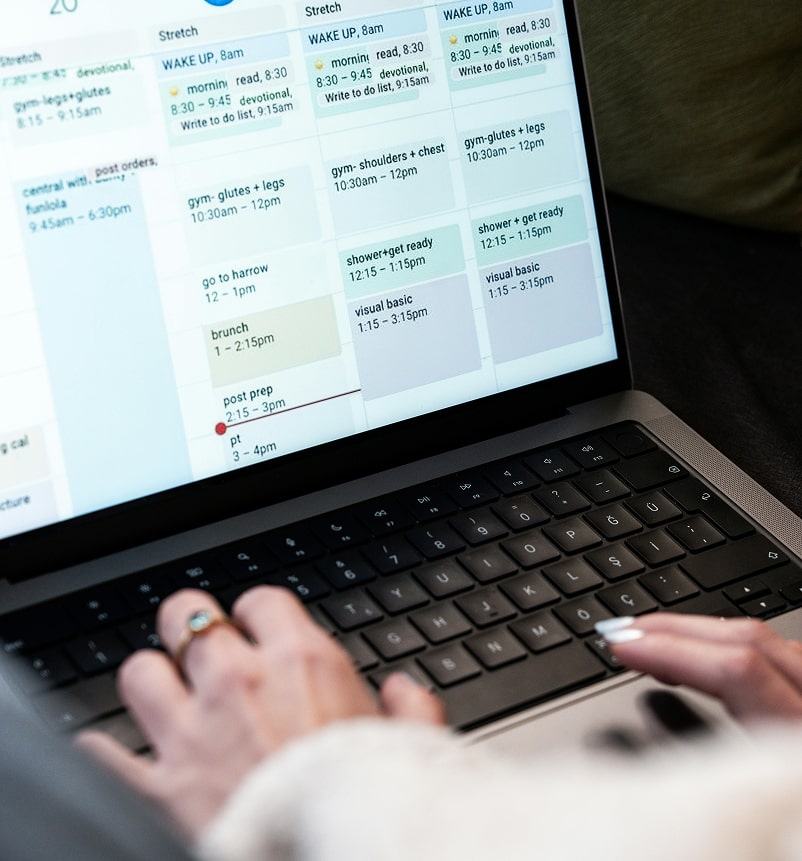 A person types on a laptop displaying a colorful daily schedule, including fitness, personal tasks, and appointments.