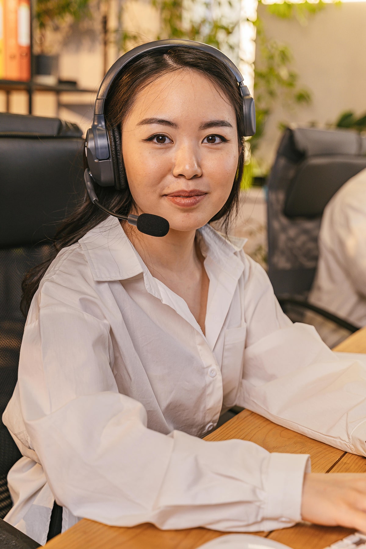 A person wearing a white shirt and headphones sits at a desk with a computer, engaged in work in an office setting.